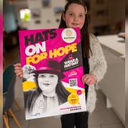 Betsy Griffin with the Wear A Hat Day poster she features on