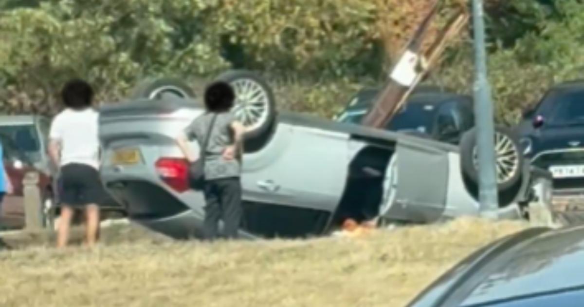 Car flipped onto roof after hitting pole, leaving driver trapped and wiring exposed