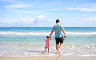 A father with his daughter walking on a beach (Canva)